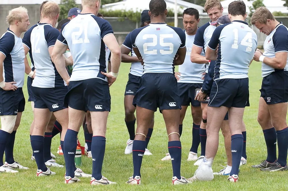 Football team huddle on a training pitch, coaching staff talking to players, bri