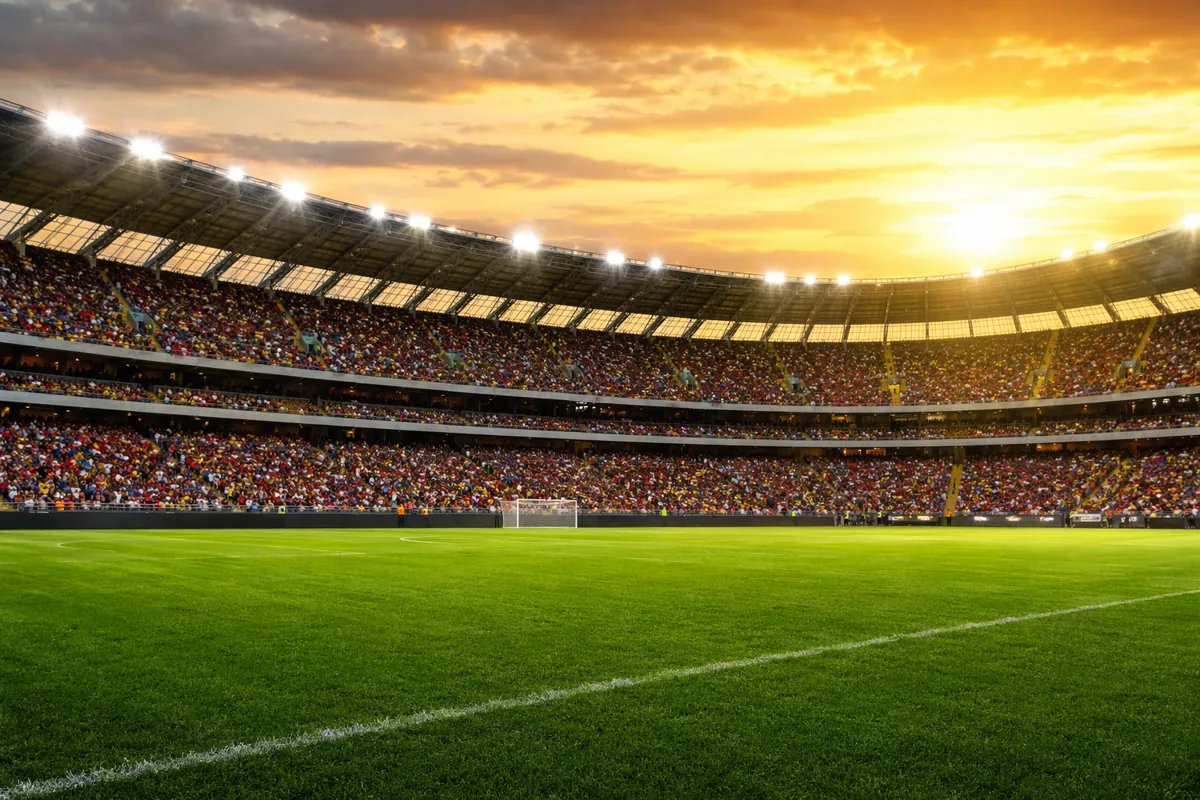 Wide shot of a generic football stadium during golden hour, with blurred fans wearing colo