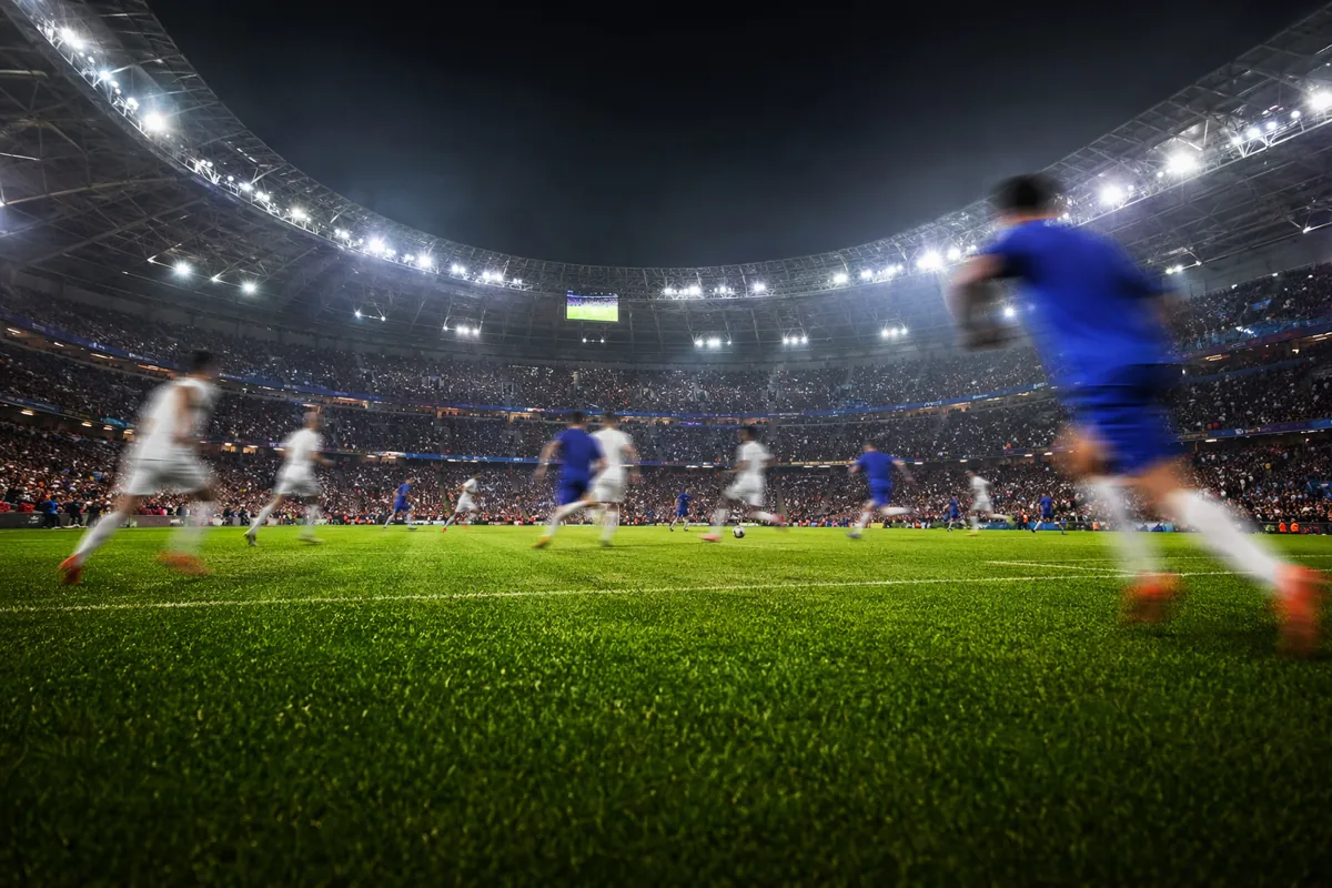 Wide shot of a professional football stadium during a high-intensity match, blurred player