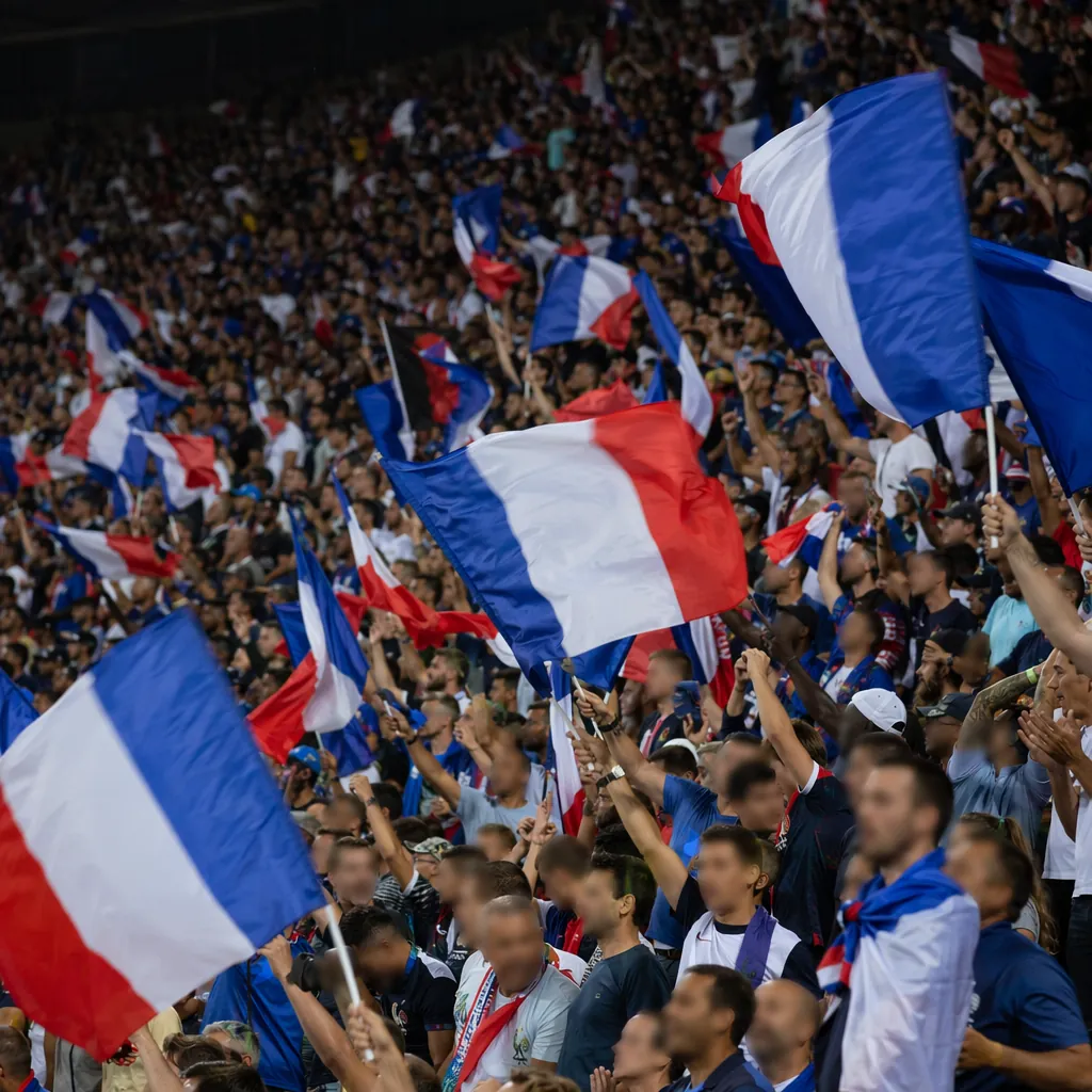 Wide shot of football fans waving national flags in stadium stands, blurred face