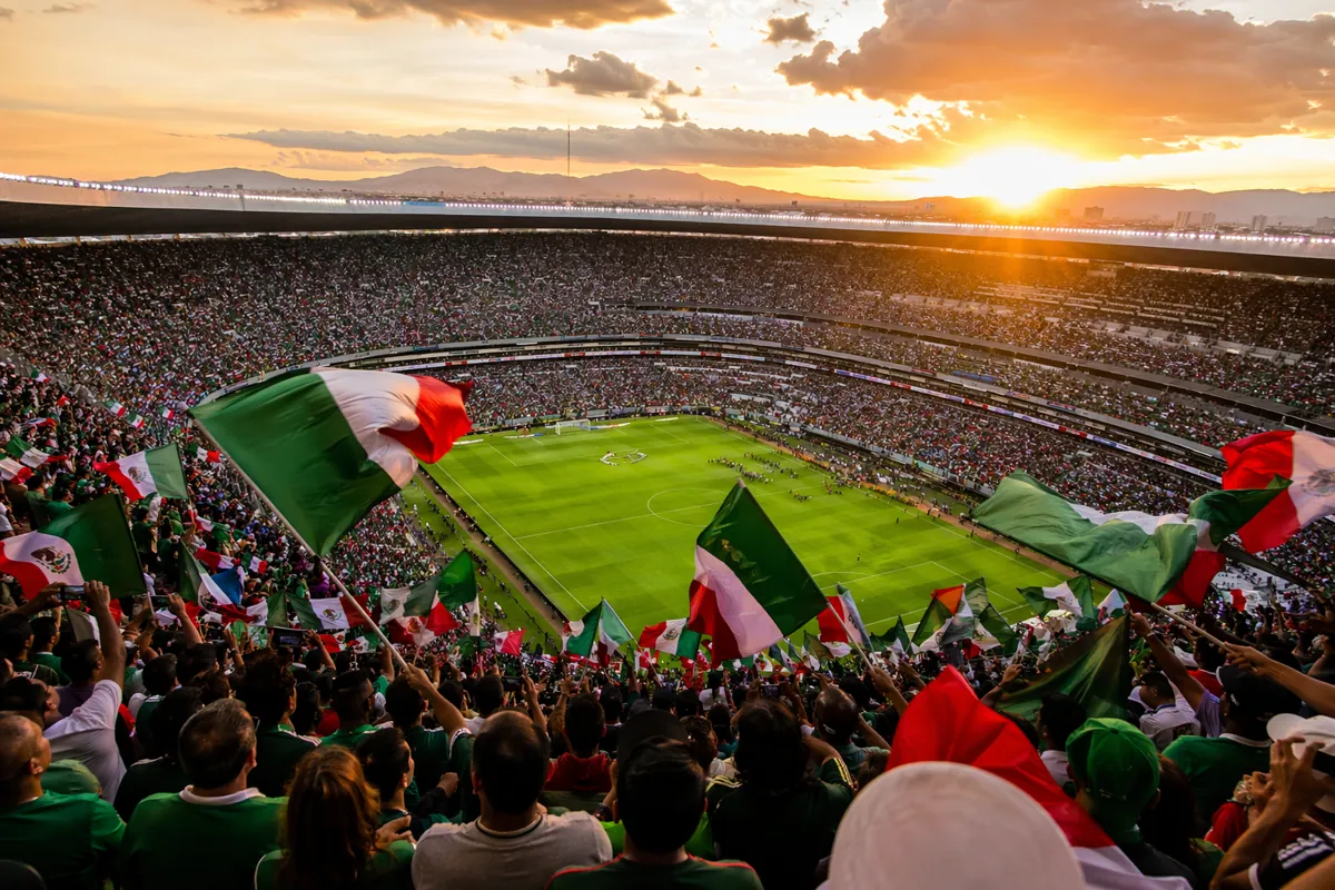 Wide shot of packed iconic football stadium in Mexico City, vibrant pre-match atmosphere,