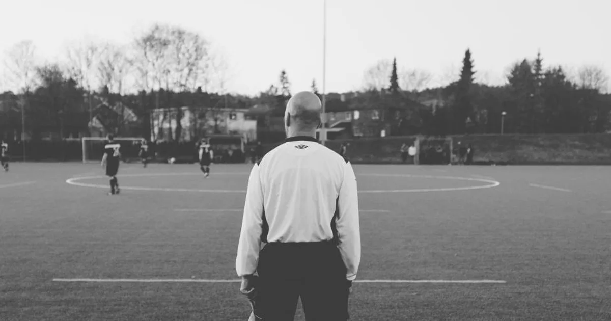 Professional football referee holding a whistle standing on a green World Cup football fie