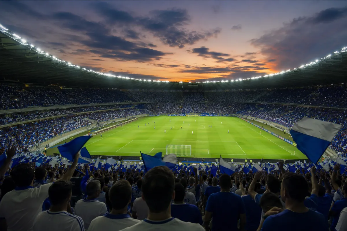 Wide shot of a professional football stadium at dusk, filled with cheering fans wearing bl