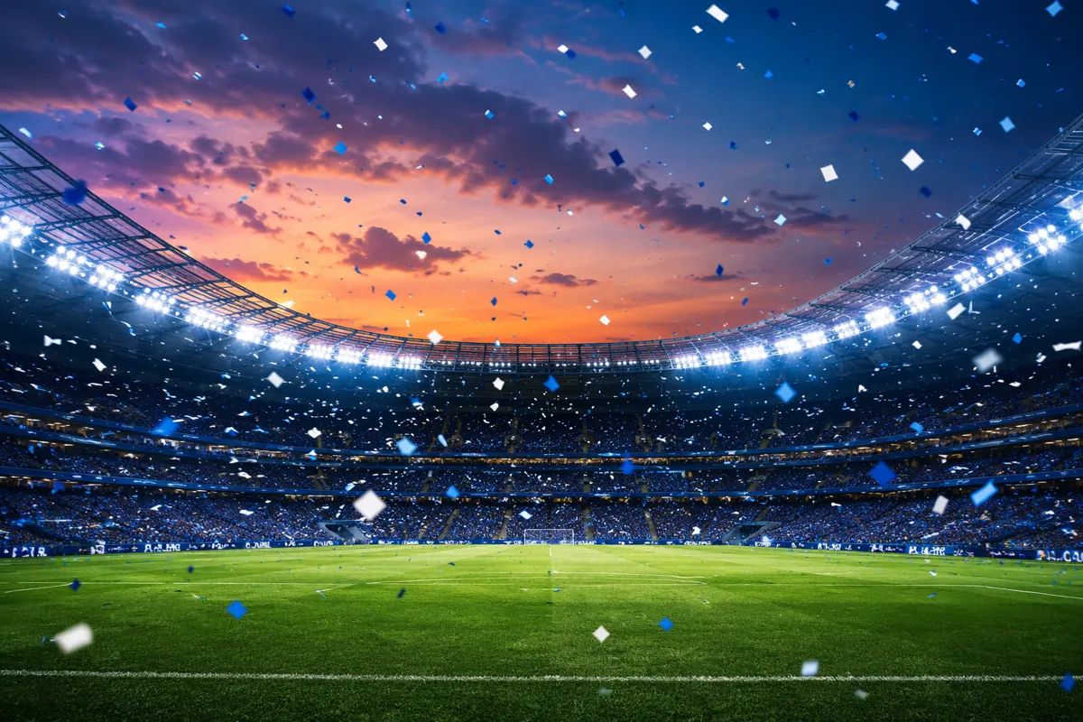 Professional football stadium at dusk, blue and white confetti falling, empty green pitch