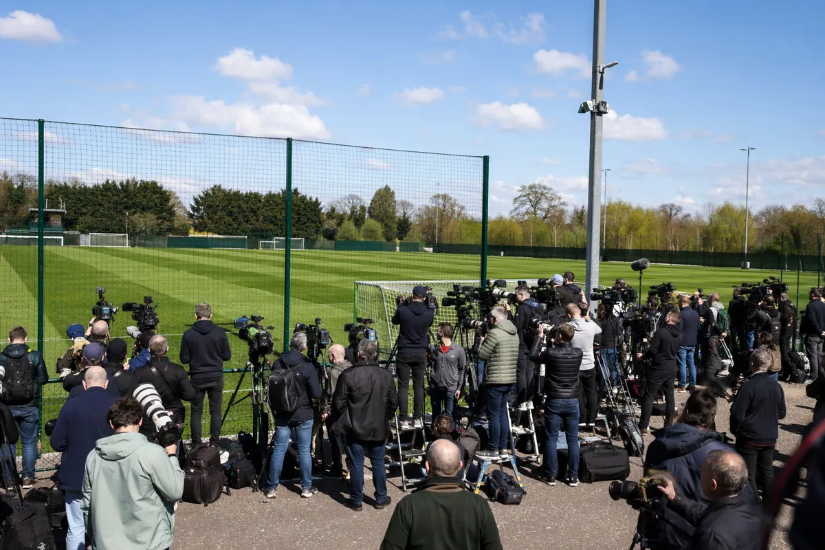 Wide shot of a professional football training ground, dozens of journalists holding camera