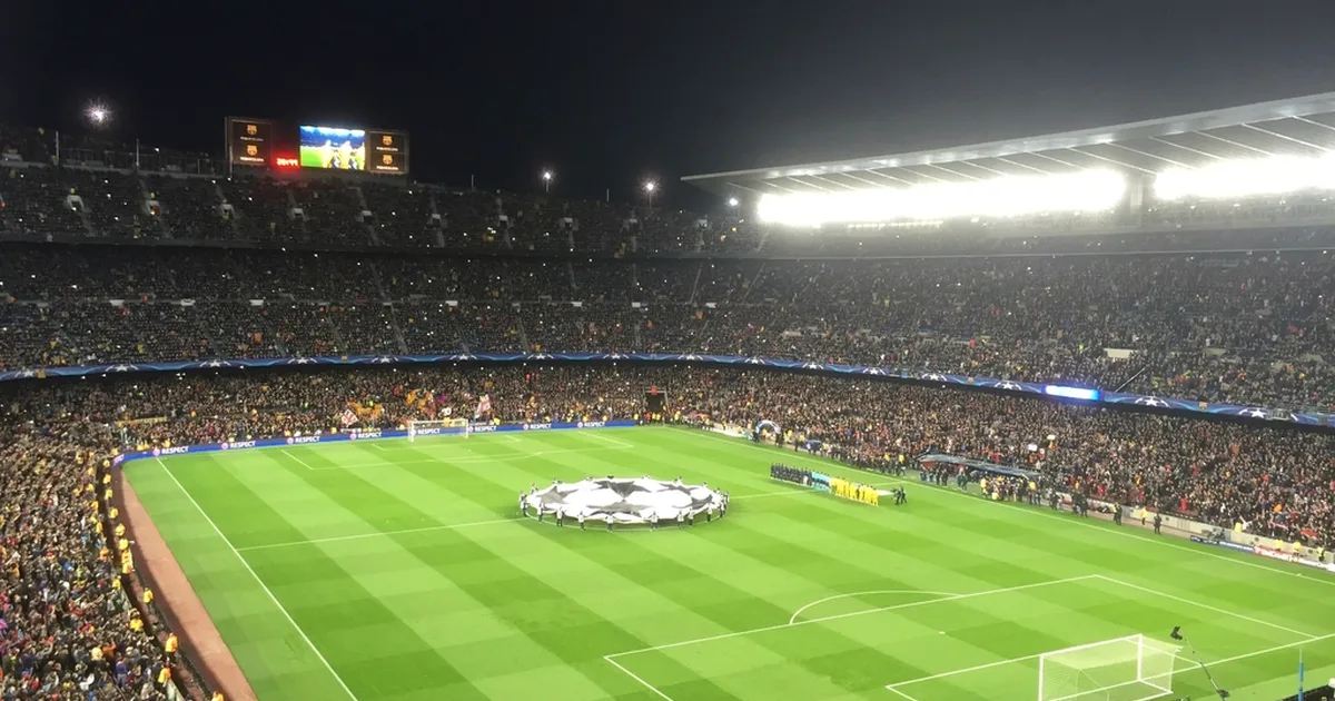 Wide shot of a fully packed modern football stadium at dusk, bright floodlights illuminati