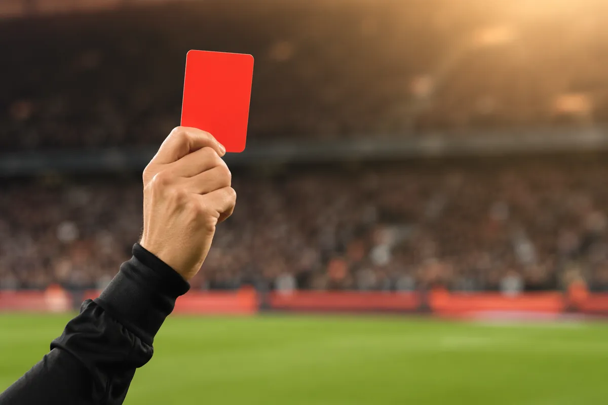 Close-up shot of a red card held up by a professional football referee on a green football