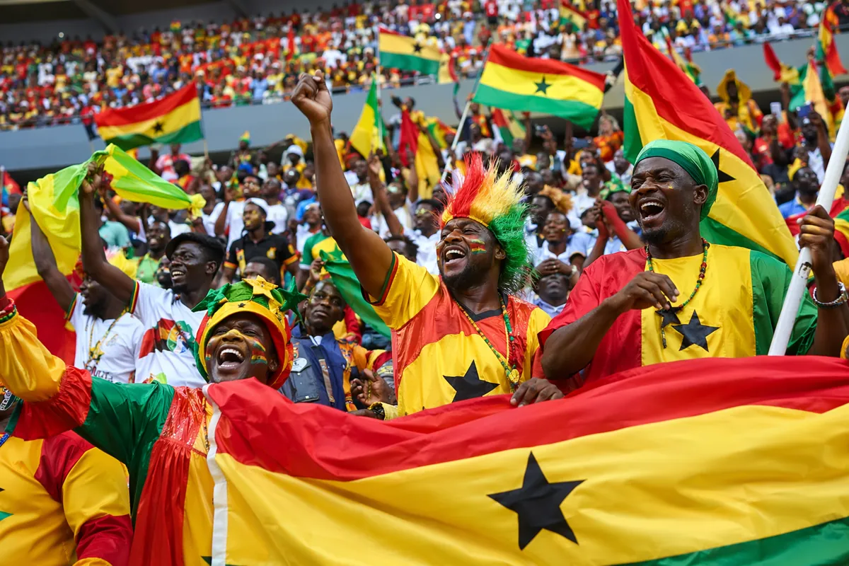 Wide shot of vibrant African football fans waving colorful national flags in stadium stand