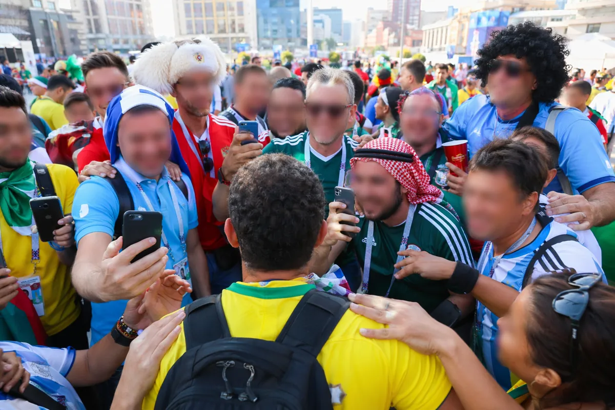A crowded street scene in a World Cup host city, many football fans in colorful jerseys ga