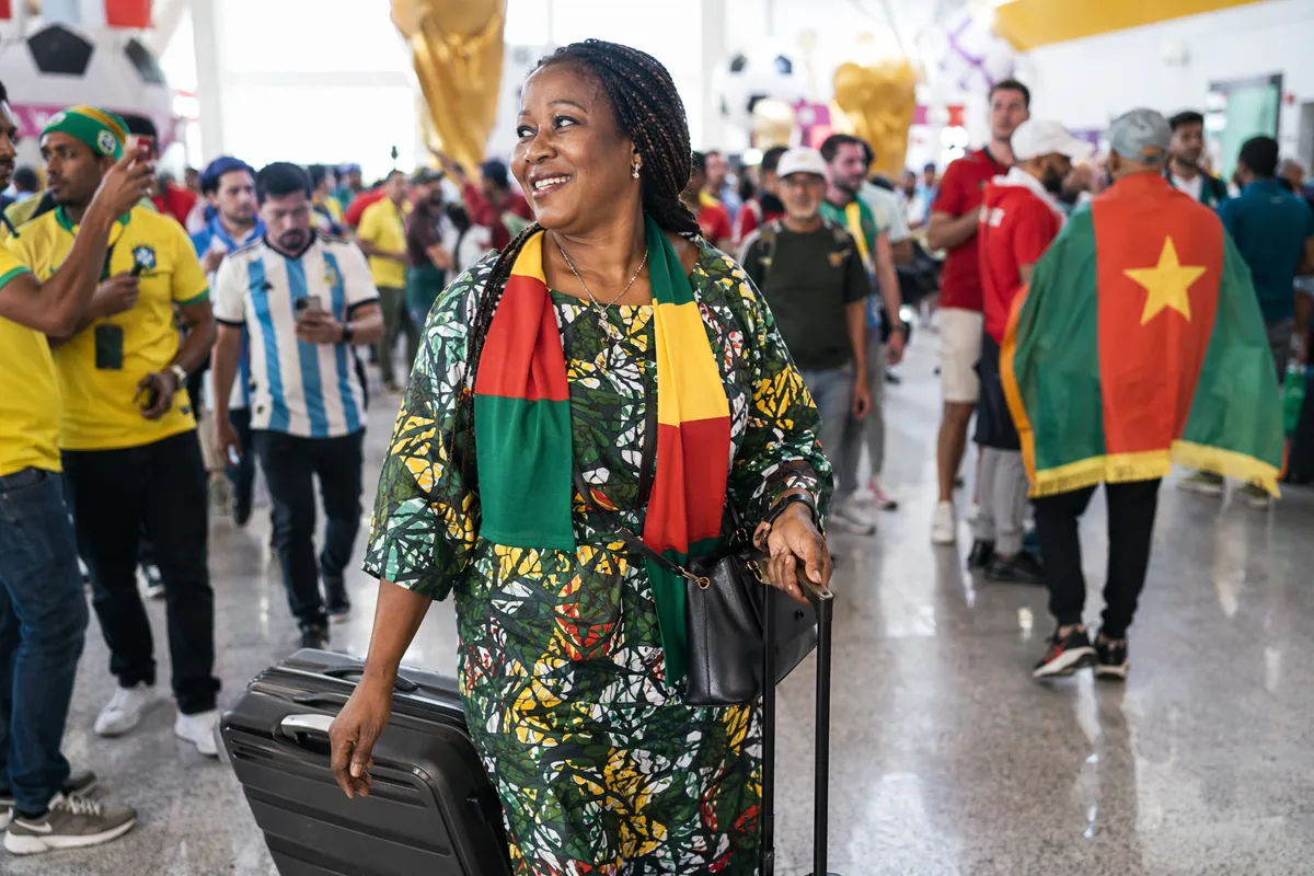 A smiling middle-aged African woman pulling a large rolling suitcase at a busy internation