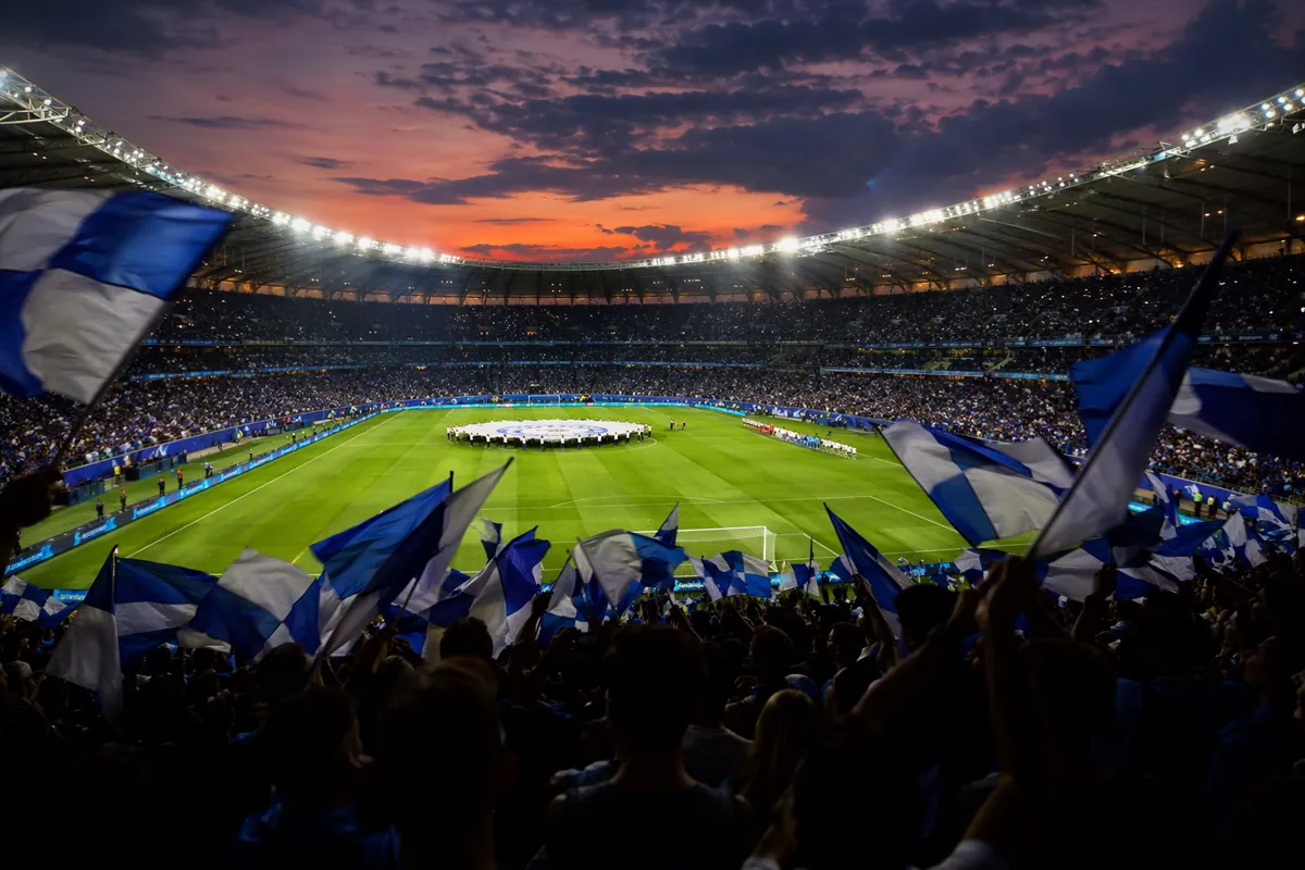 Wide shot of a professional football stadium at dusk, green pitch under bright stadium lig