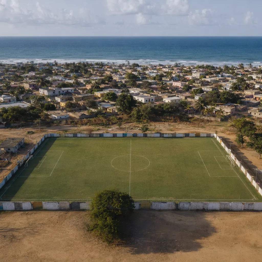 Aerial view of a small local football pitch in a coastal African town, blue ocea
