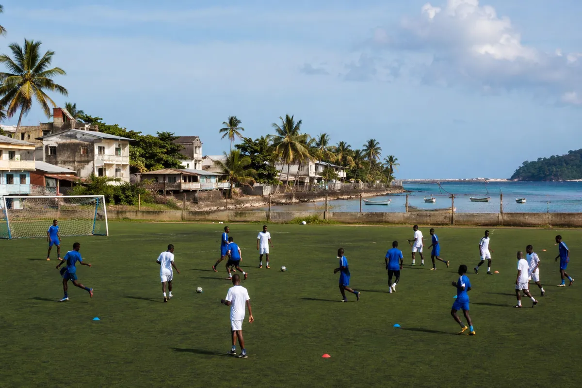 Wide shot of a generic football pitch in a small coastal African town, group of anonymous