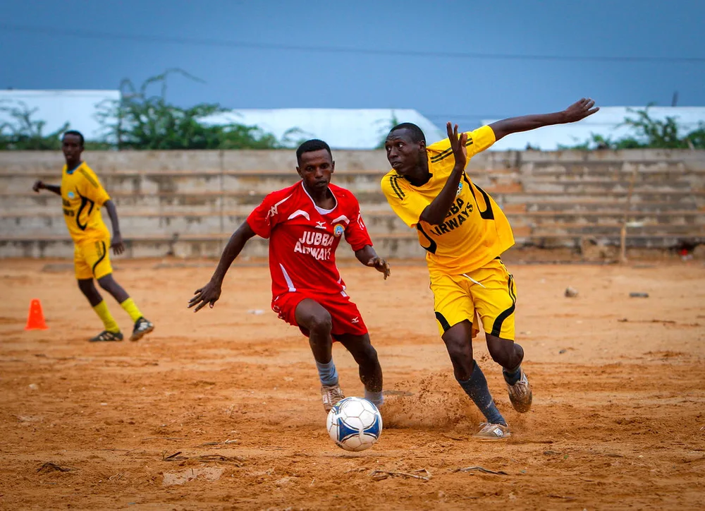 Blurred action shot of a football match in progress, wide view of players runnin