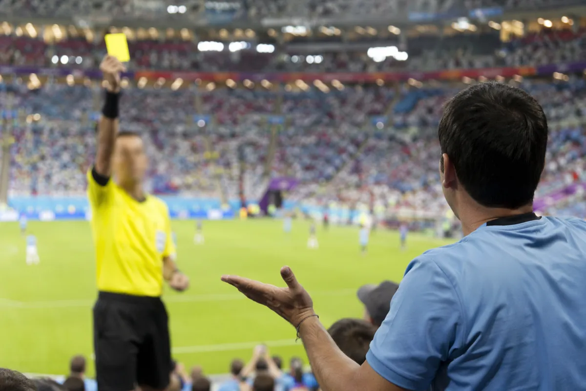 Professional editorial news photo, blurred football referee holding a yellow card towards