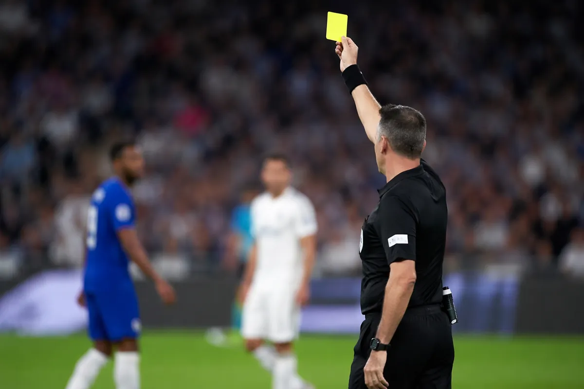 Professional football referee holding yellow card on green football pitch during official
