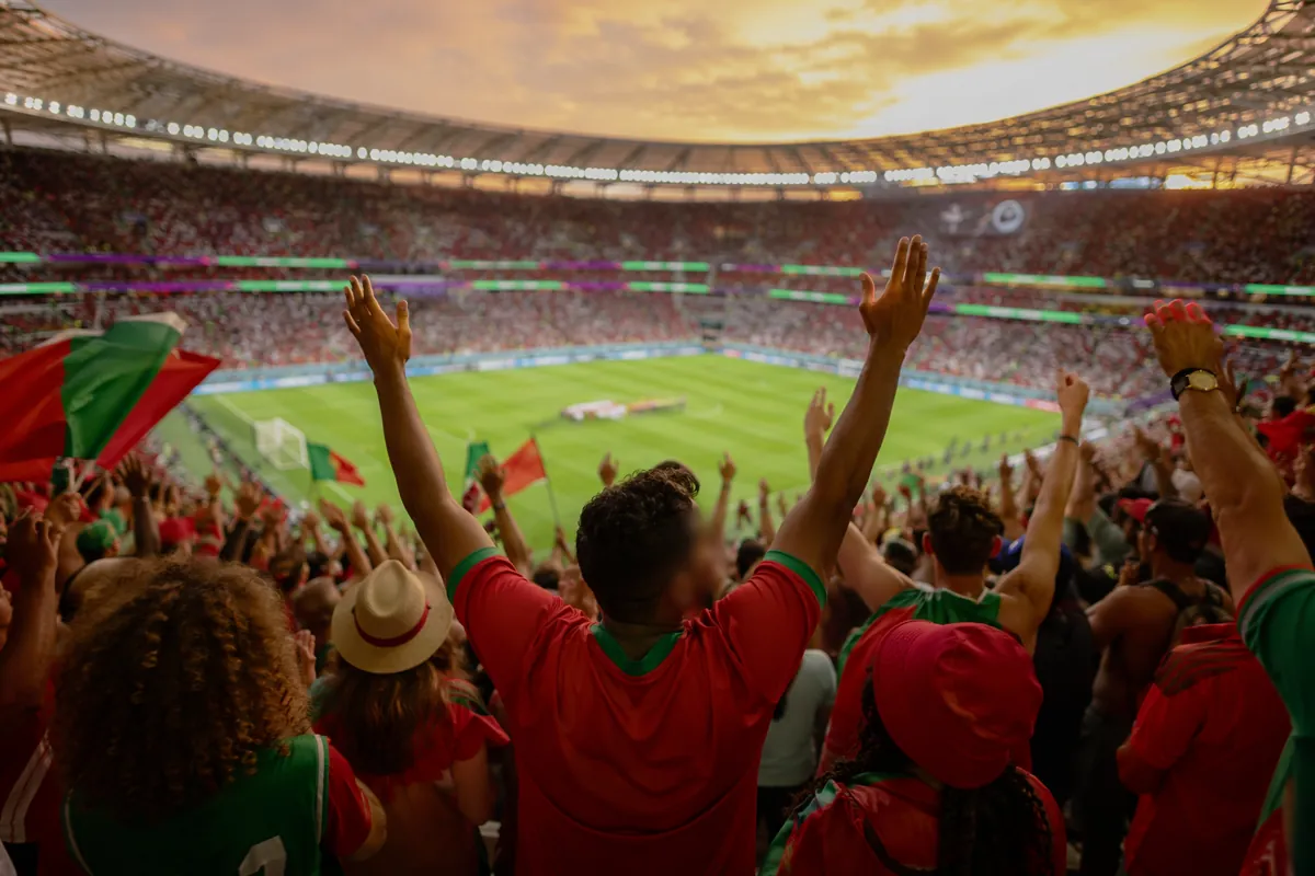 Wide shot of diverse football fans cheering in a modern World Cup stadium, blurred faces,