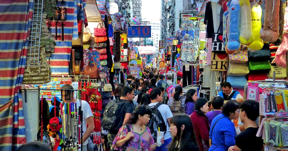 Wide shot of a traditional Hong Kong wet market with fresh produce stalls, warm daylight,
