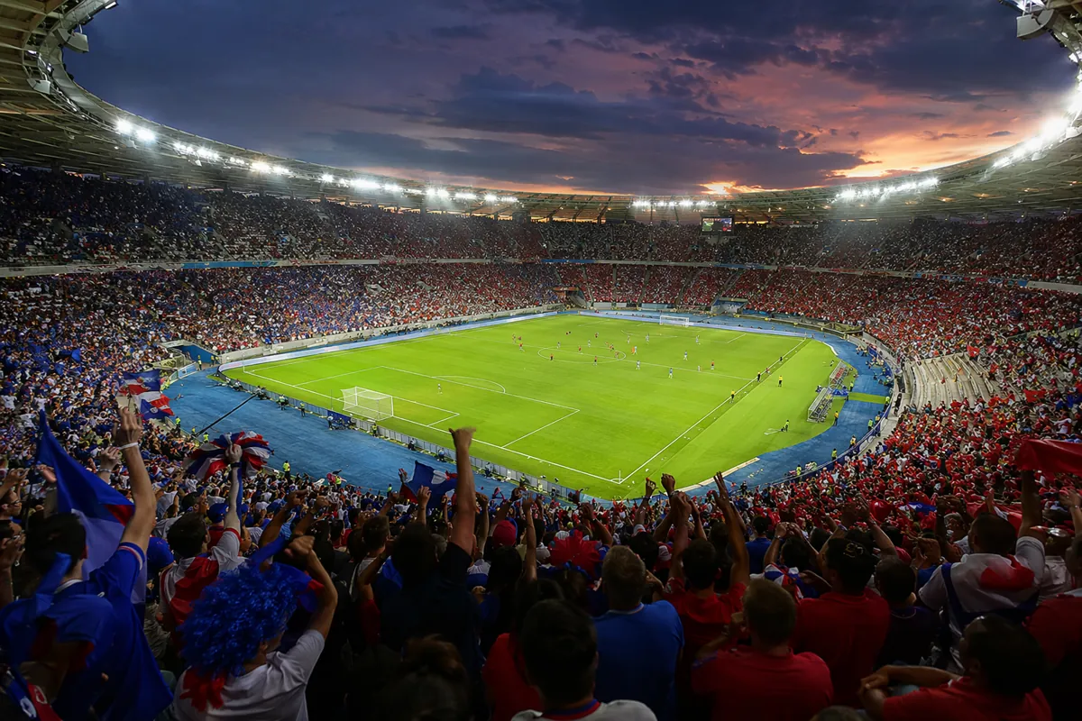 Wide shot of a packed FIFA World Cup football stadium at dusk, bright floodlights illumina