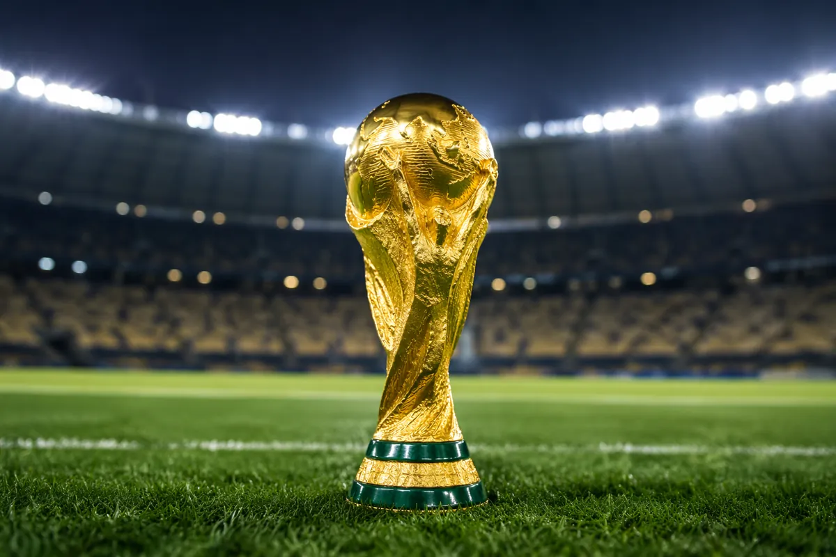 Golden football trophy on green soccer pitch with blurred stadium floodlights in backgroun