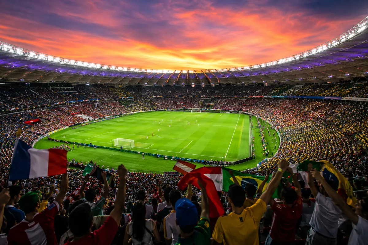 Wide shot of a modern football stadium at dusk, filled with colorful cheering fans, bright
