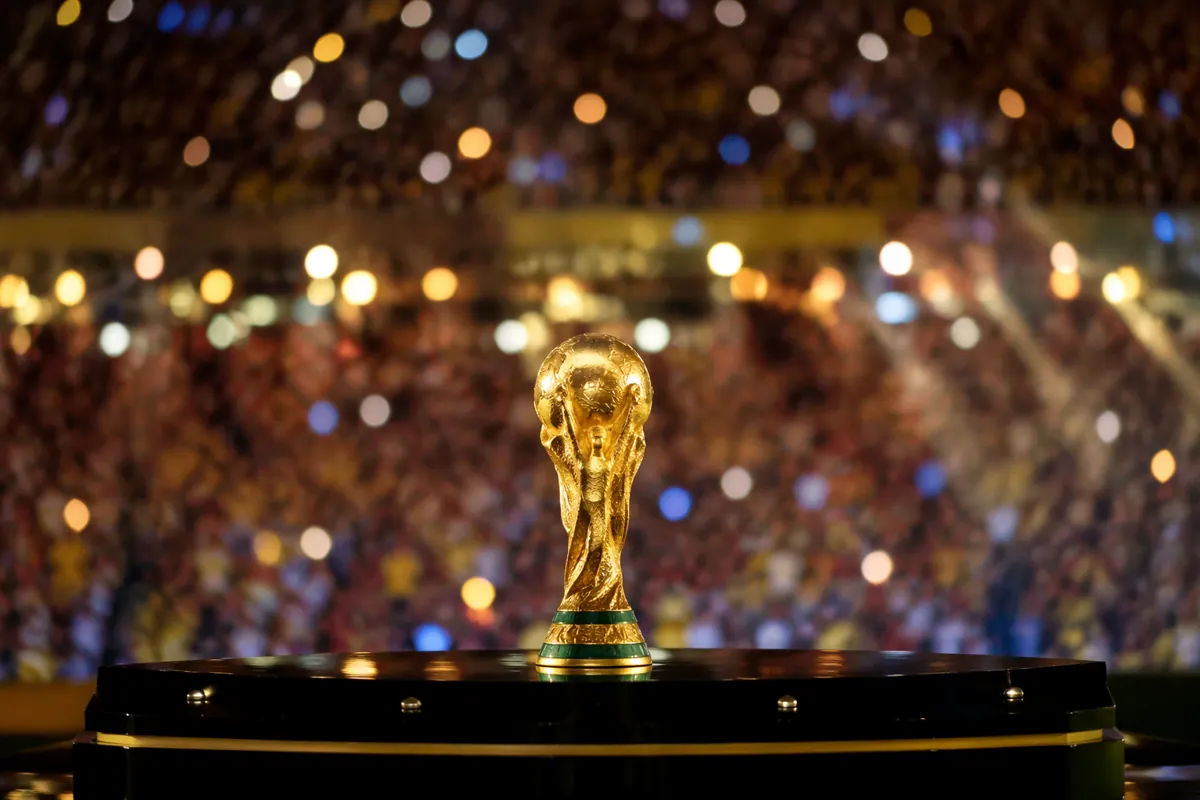 A wide shot of a glowing World Cup trophy on a polished dark stage, surrounded by soft col