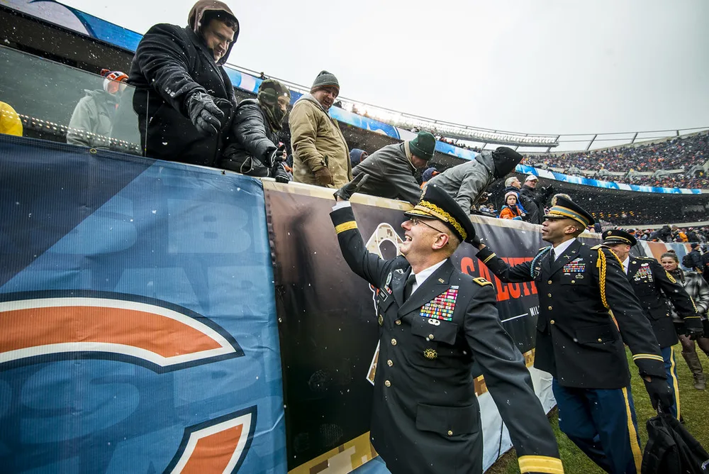 Close-up shot of a generic football match sideline, blurred silhouettes of footb