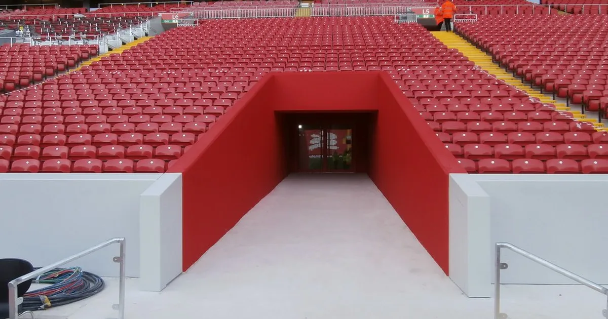 Wide shot of a professional football stadium tunnel with dim ambient lighting, neutral pla