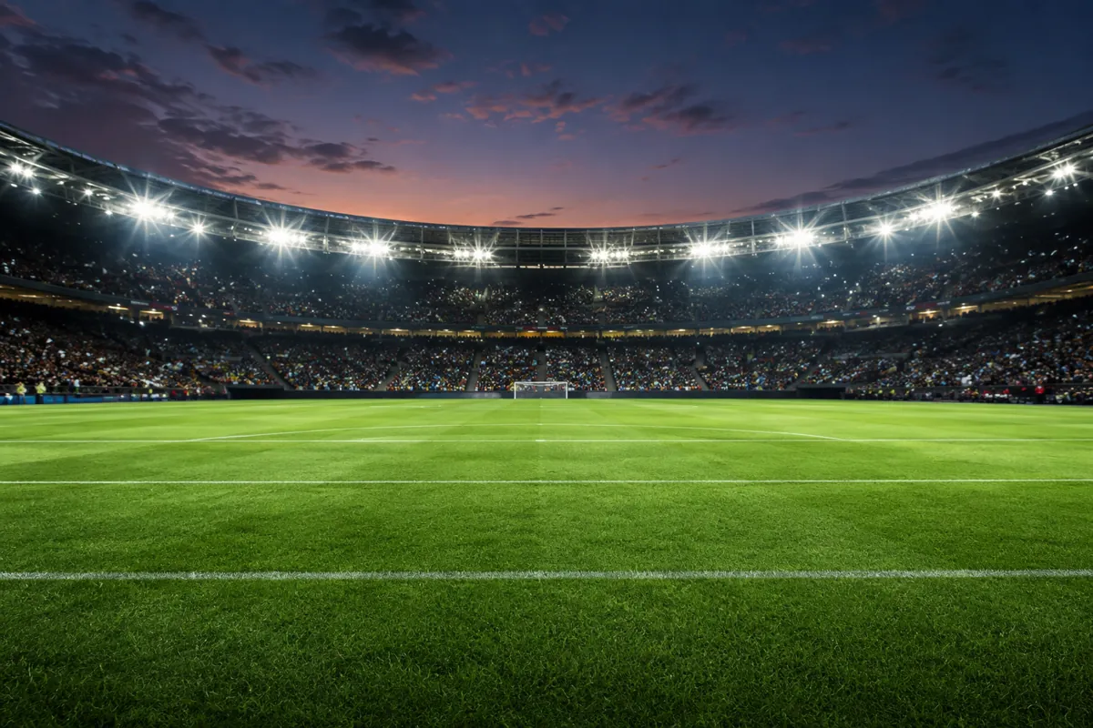 Wide shot of a well-maintained green football pitch under bright stadium floodlights at du