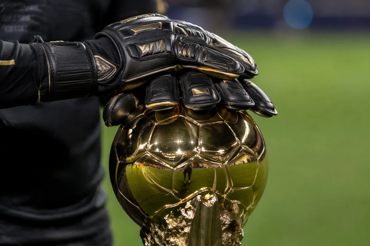 Close up shot of a professional goalkeeper's gloved hands resting on a golden football tro