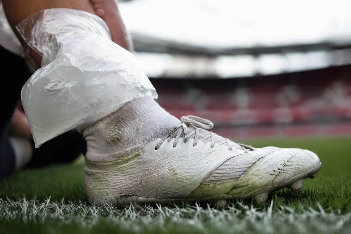Close up shot of a professional football player's boots with an ice pack placed on an ankl