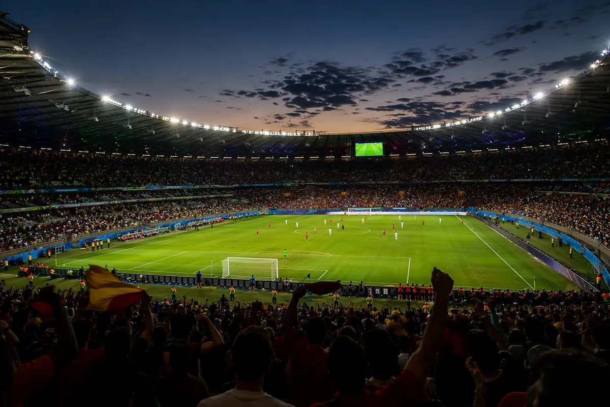 Wide shot of a professional football stadium at dusk, bright stadium lights illuminating t