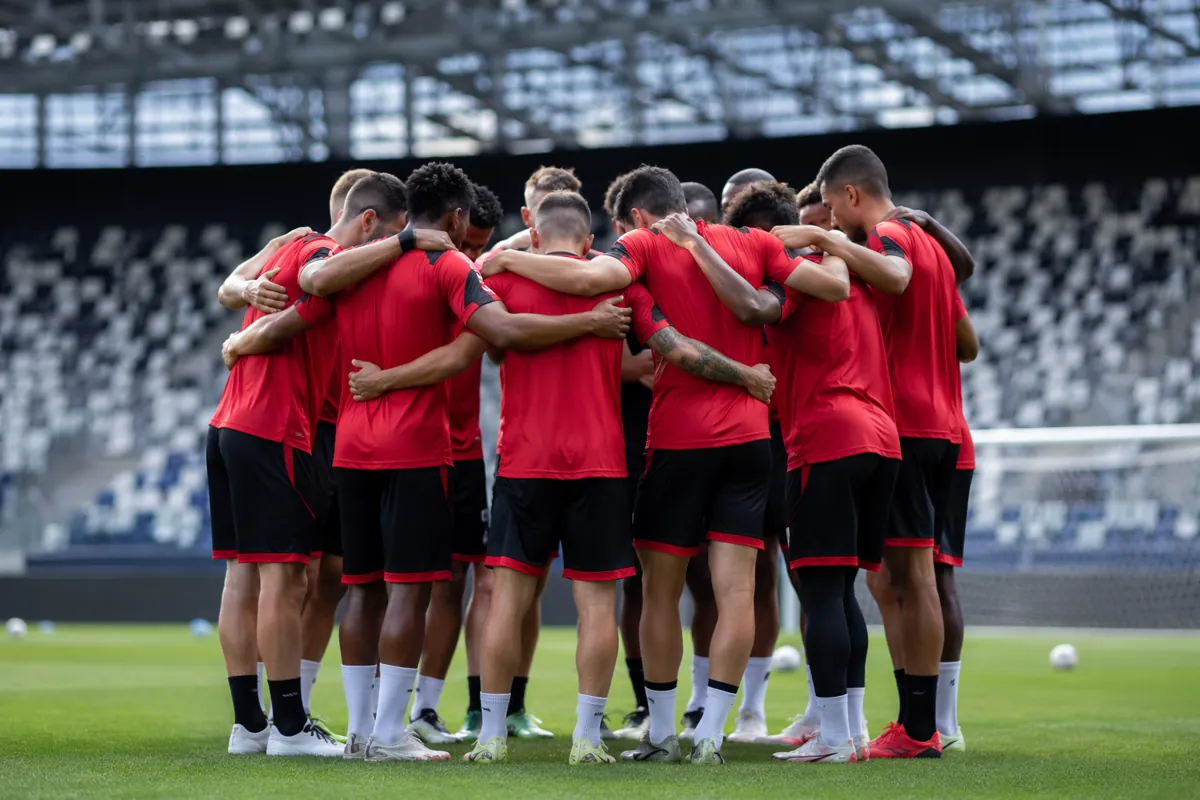Wide shot of a group of football players in generic red and black training kits huddling o