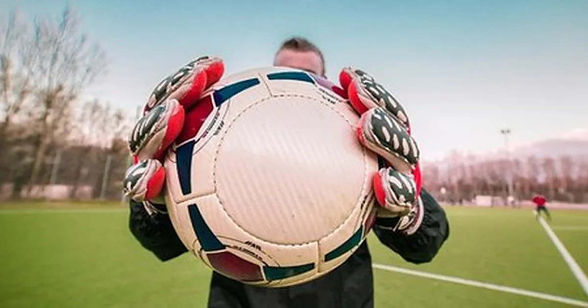 Professional football goalkeeper gloves placed on a well-maintained green grass pitch, wit