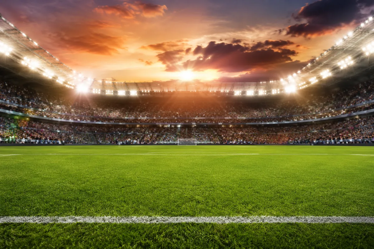 Wide shot of a green World Cup football field under bright stadium lights, blurred crowd o