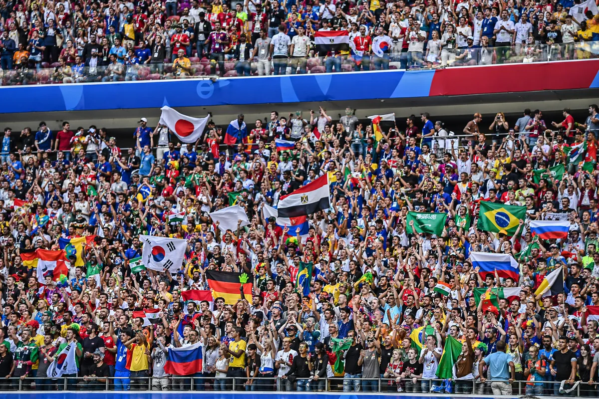 Wide shot of a World Cup football stadium stands, diverse fans waving national flags, vibr