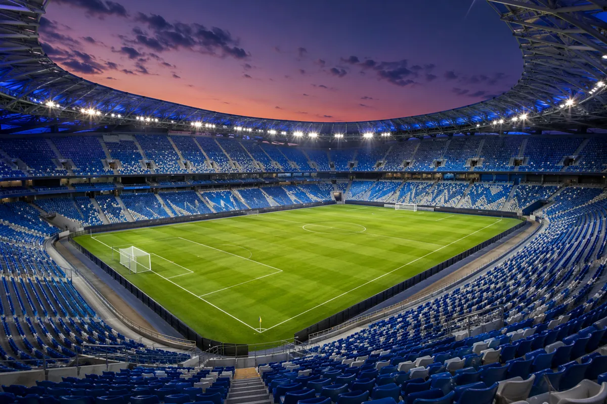 Wide shot of a modern FIFA World Cup football stadium at dusk, bright floodlights illumina