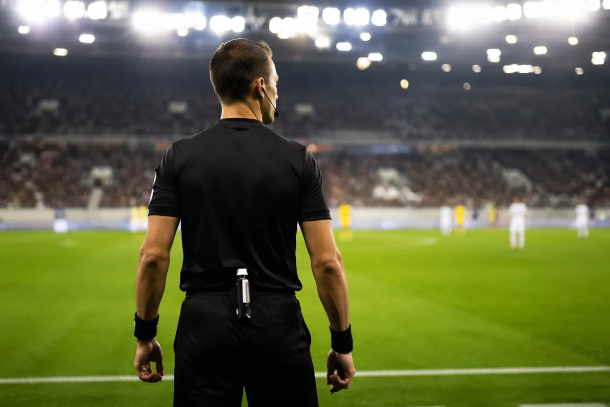 Professional male soccer referee wearing black uniform standing on a well-maintained green