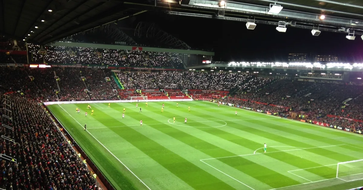 Professional football editorial header image, empty Old Trafford stadium on a sunny match