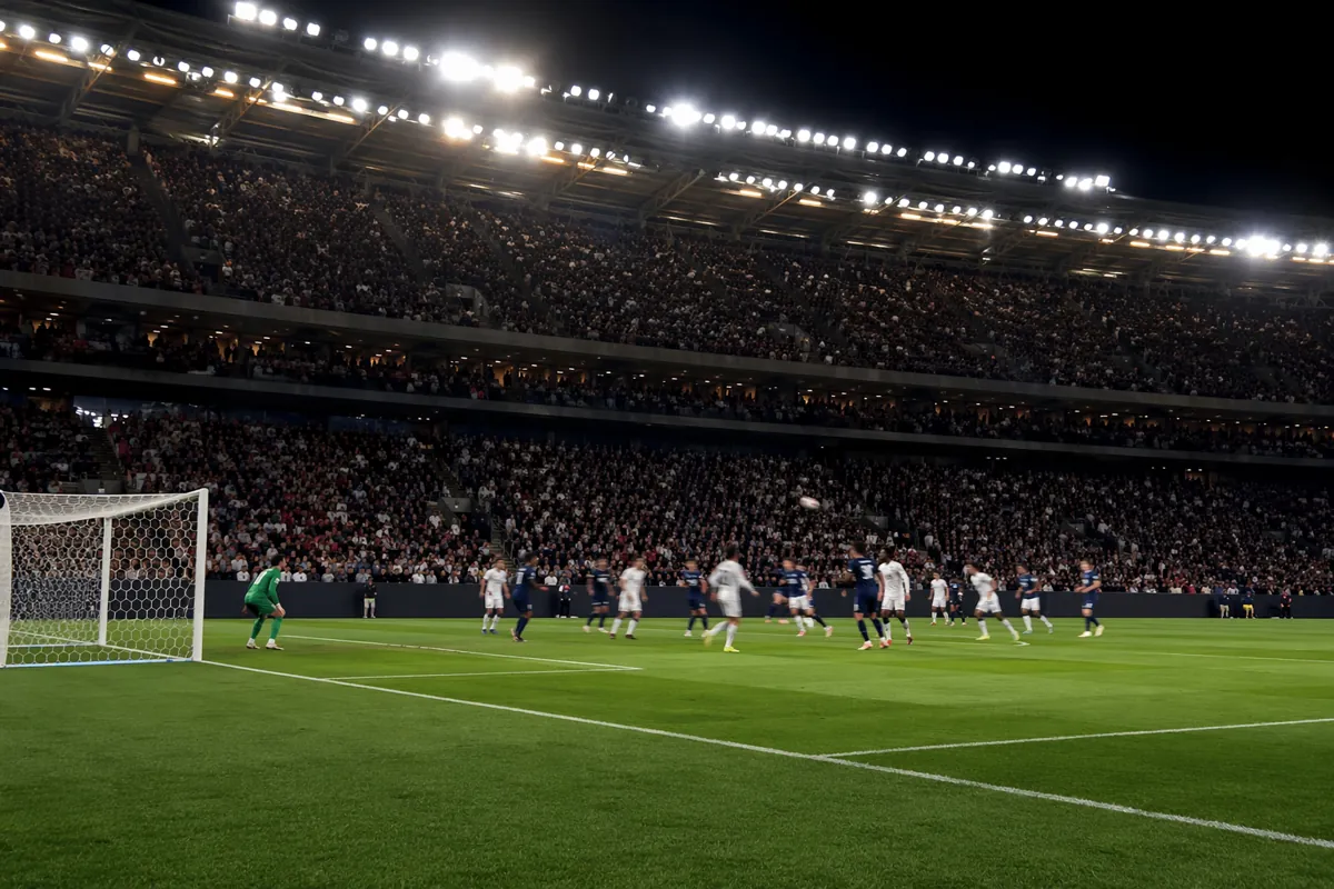 A wide shot of a professional football stadium during a pre-World Cup warm-up match, brigh