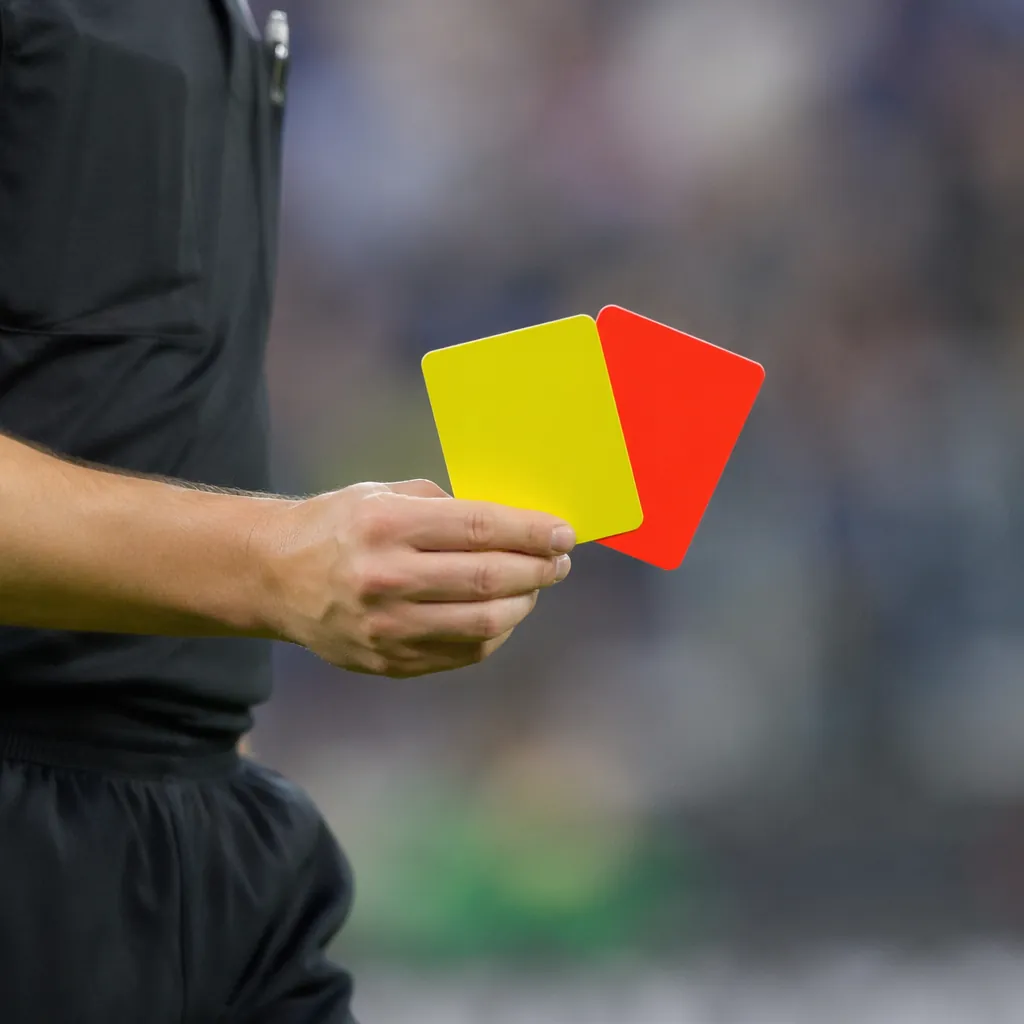 Close up shot of a referee holding a yellow card and red card on a football pitc