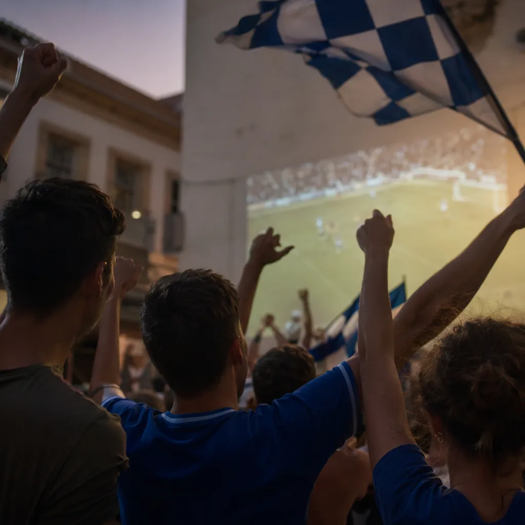 Close up of football fans cheering and waving flags while watching an outdoor pr