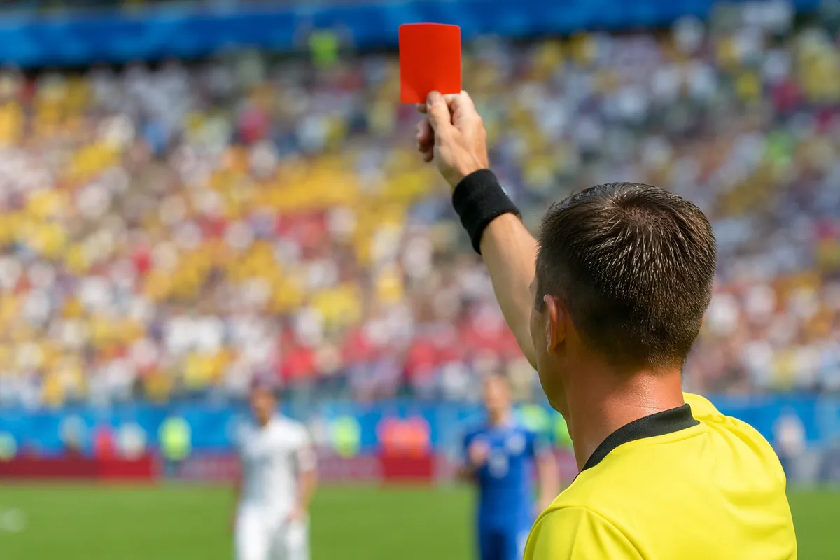 Professional sports news header image, close-up of a referee holding a red card in a sunny
