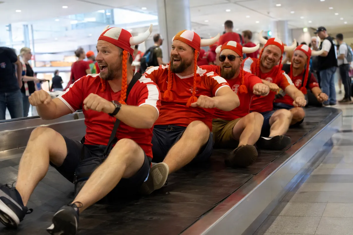 Group of football fans in red jerseys and viking horned hats pretending to row on airport