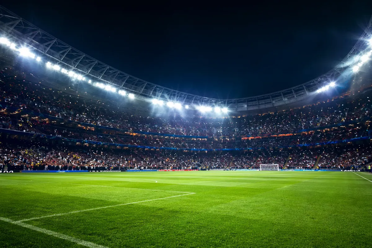 Wide shot of a professional football stadium during a night match, bright stadium lights,