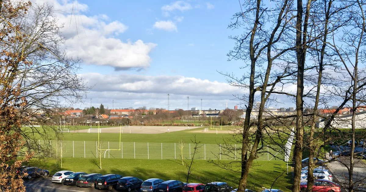 Wide shot of a modern football stadium at dusk, warm golden light illuminating the green p