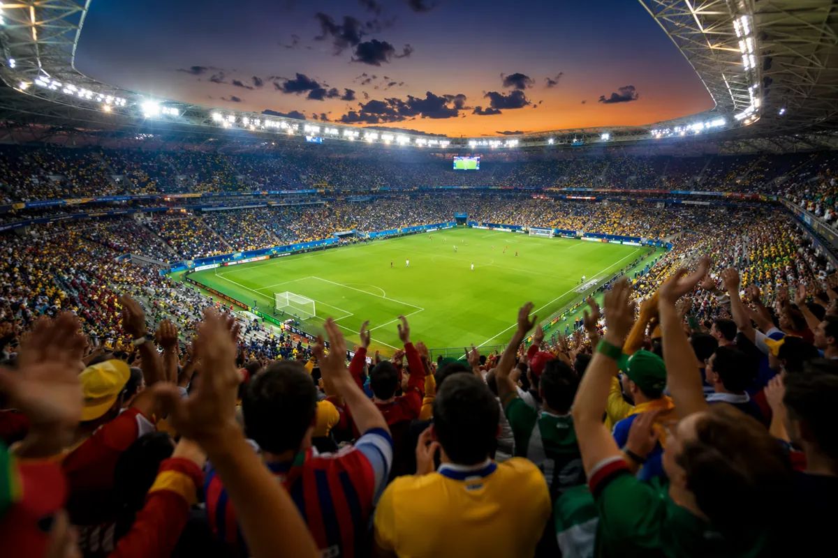 Wide shot of a packed FIFA World Cup stadium at dusk, bright stadium lights illuminating t