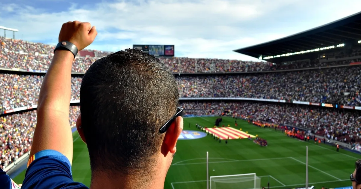 Vibrant wide shot of football fans wearing red and yellow jerseys cheering in a stadium, g