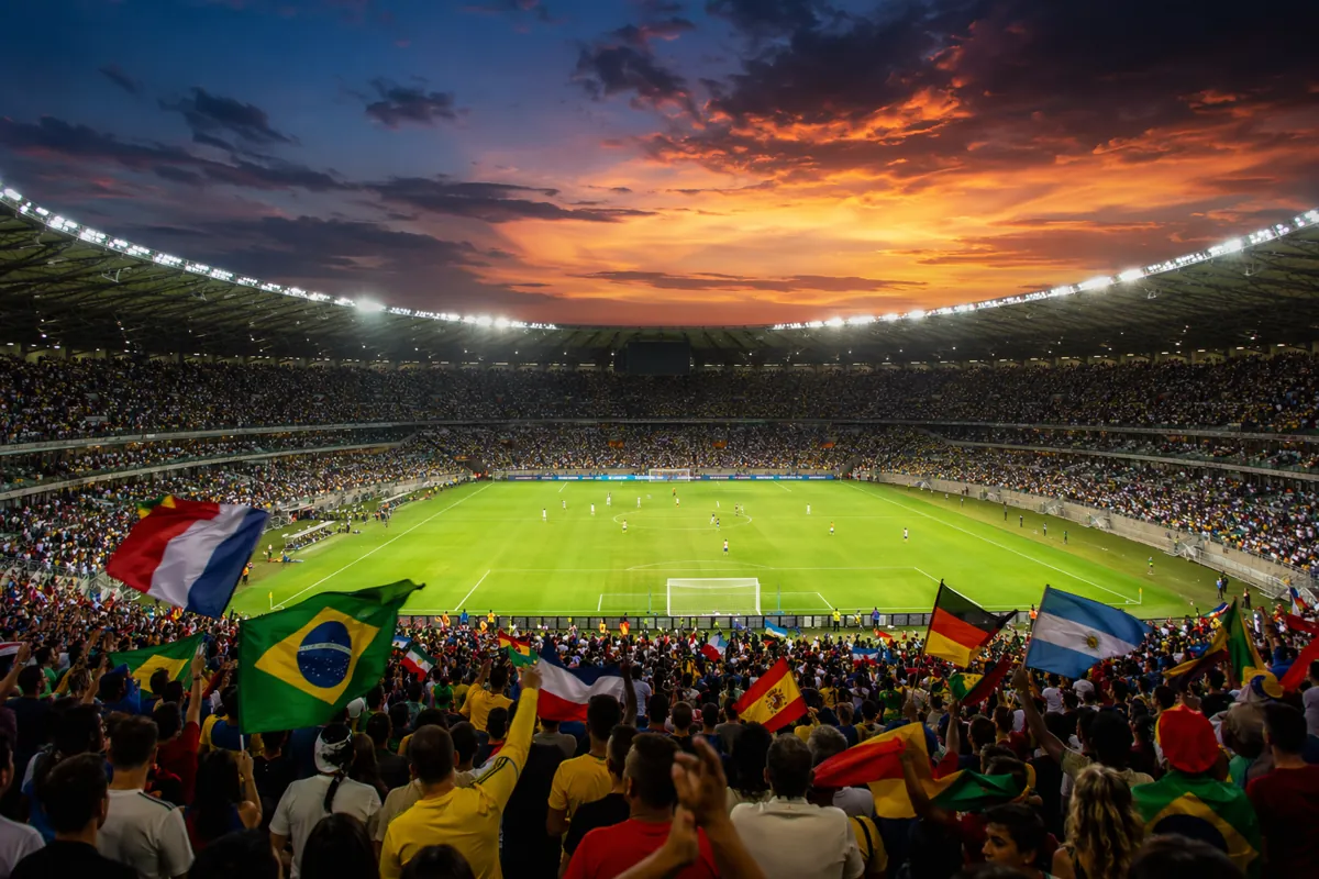 Wide shot of a vibrant football stadium at dusk, packed with cheering fans waving national