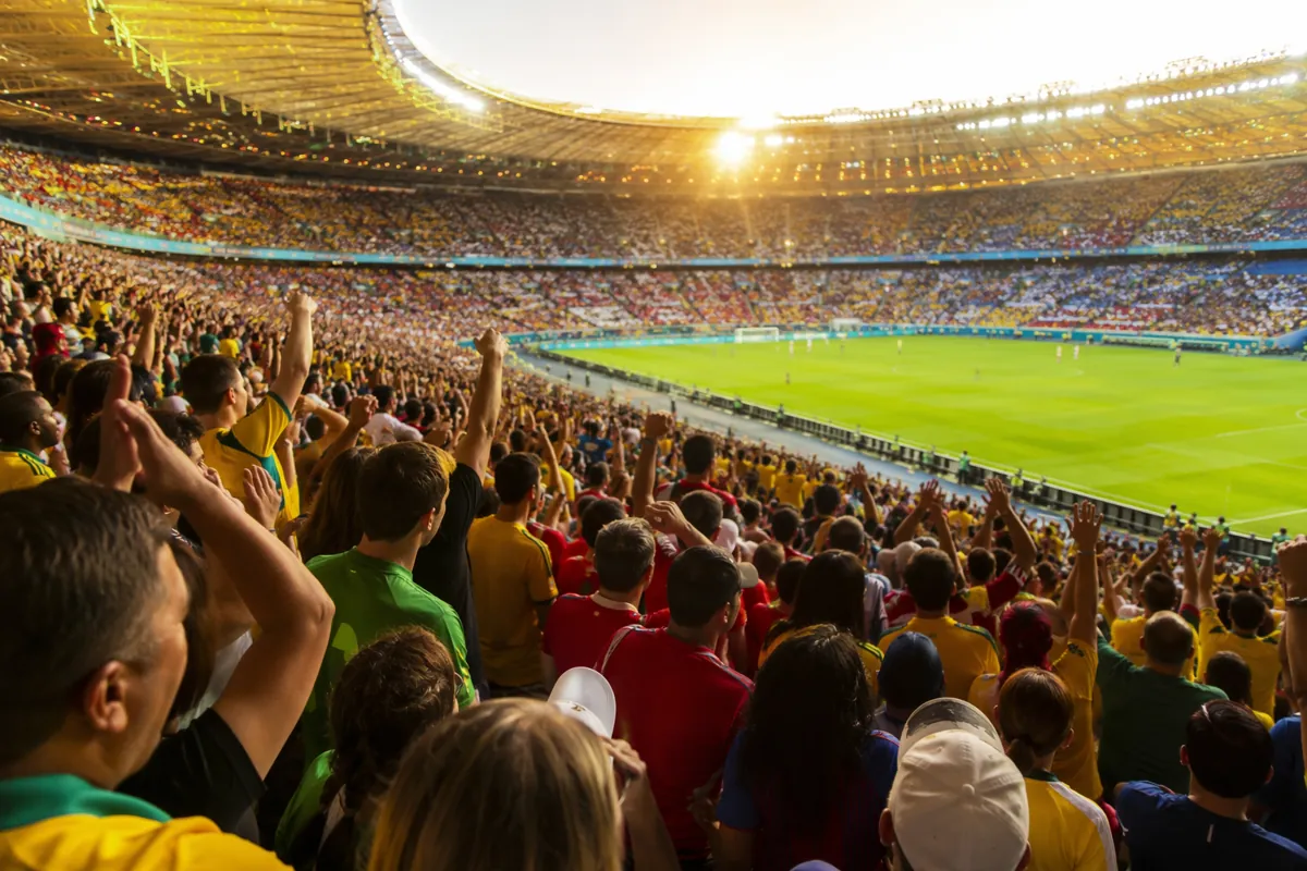 Wide shot of a packed world cup final stadium grandstand during golden hour, blurred crowd
